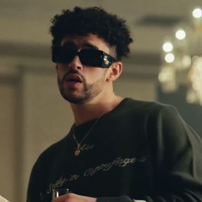 Bad Bunny or Benito Antonio Martínez Ocasio posing for a picture wearing dark sunglasses and with a glass of wine in his hand.